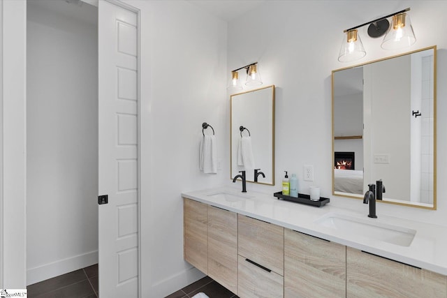 full bathroom featuring a lit fireplace, double vanity, a sink, and tile patterned flooring