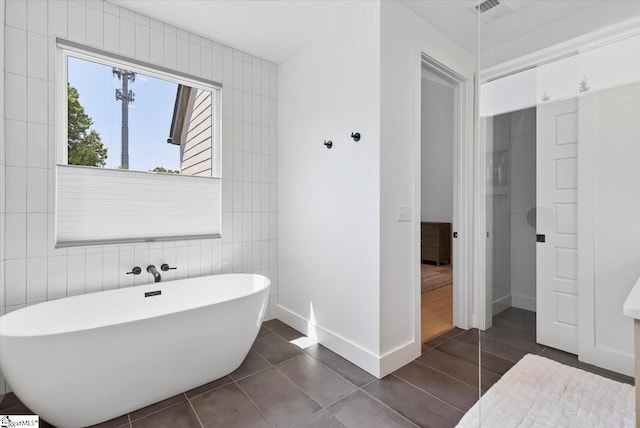 full bathroom featuring baseboards, tile patterned floors, visible vents, a freestanding bath, and tile walls