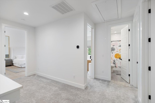 corridor featuring light colored carpet, attic access, baseboards, and visible vents