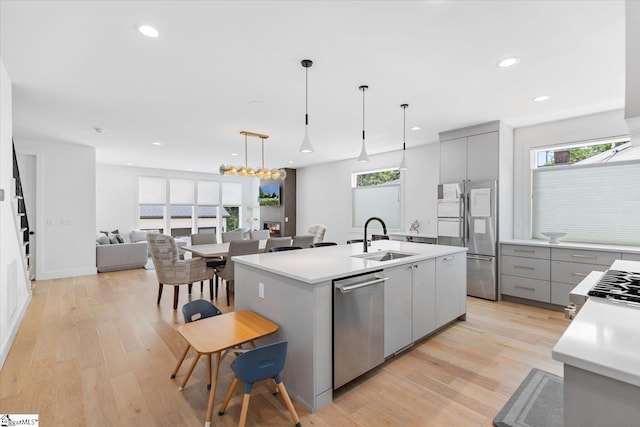 kitchen with a sink, appliances with stainless steel finishes, an island with sink, gray cabinets, and light wood-style flooring