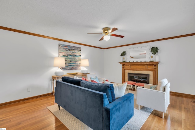 living area with baseboards, a ceiling fan, crown molding, light wood finished floors, and a glass covered fireplace