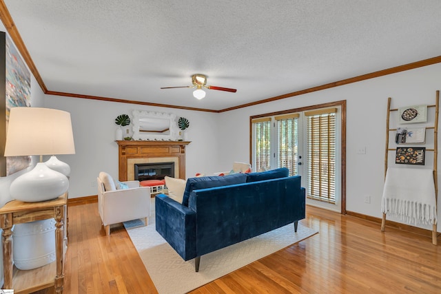 living area featuring ornamental molding, ceiling fan, a textured ceiling, light wood finished floors, and a glass covered fireplace