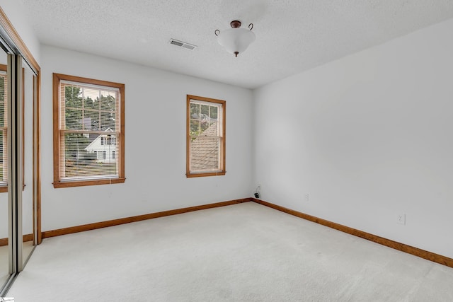 empty room with light carpet, baseboards, visible vents, and a textured ceiling