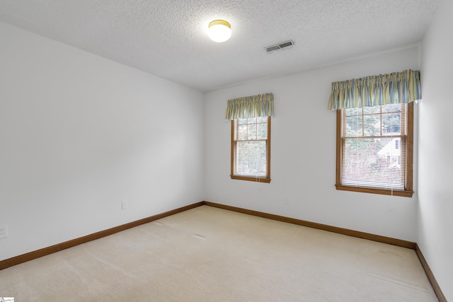 unfurnished room with light carpet, baseboards, visible vents, and a textured ceiling