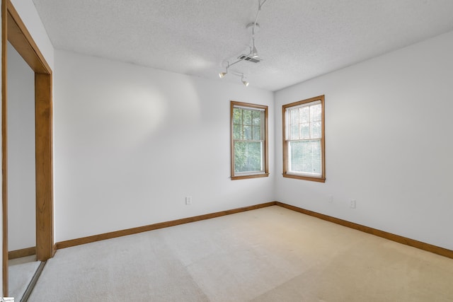 empty room with track lighting, a textured ceiling, light colored carpet, visible vents, and baseboards