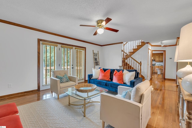 living area with a ceiling fan, ornamental molding, light wood finished floors, and stairs