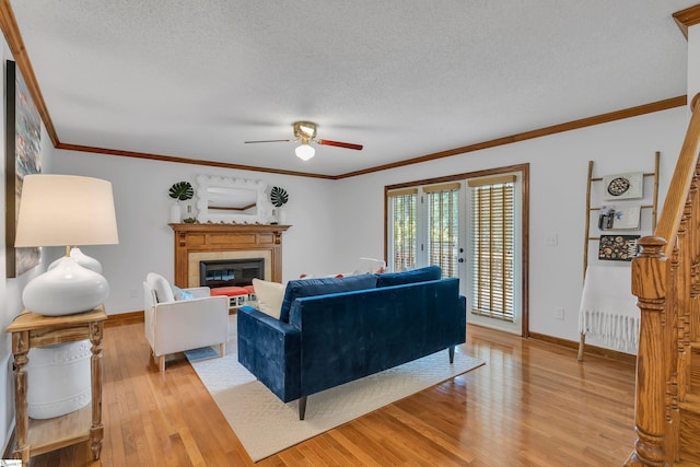living room with light wood finished floors, a textured ceiling, a ceiling fan, and ornamental molding