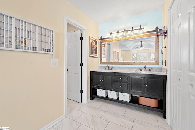 bathroom with a sink, ceiling fan, double vanity, and baseboards
