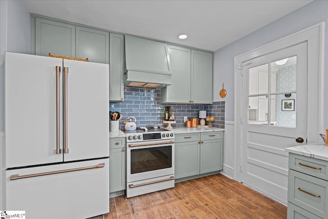 kitchen featuring white appliances, light stone counters, custom range hood, light wood finished floors, and backsplash