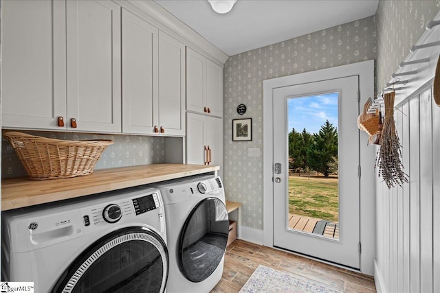 washroom featuring washer and dryer, wallpapered walls, light wood finished floors, and cabinet space