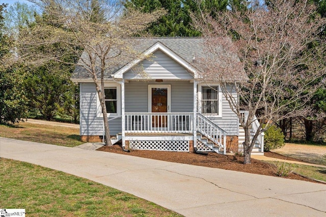 bungalow-style home with a front lawn, a shingled roof, covered porch, and crawl space