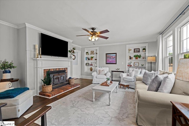 living room featuring ornamental molding, built in features, a fireplace, a ceiling fan, and wood finished floors