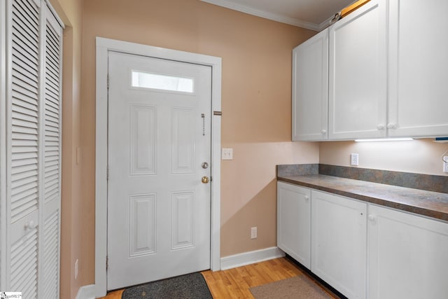 interior space featuring white cabinets, baseboards, ornamental molding, dark countertops, and light wood-style floors