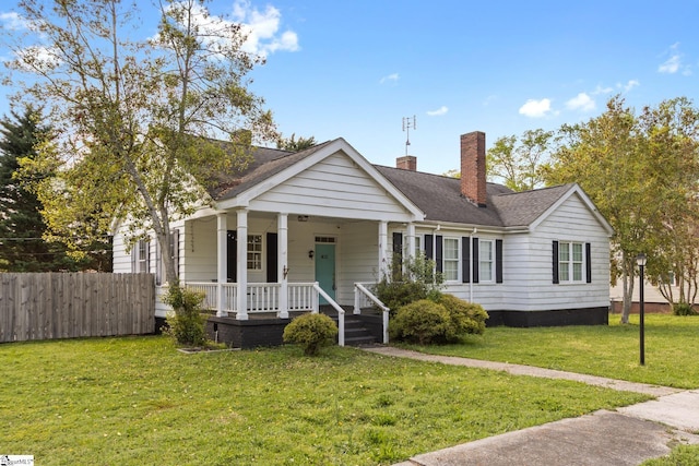 view of front of house with covered porch, roof with shingles, fence, a front lawn, and a chimney