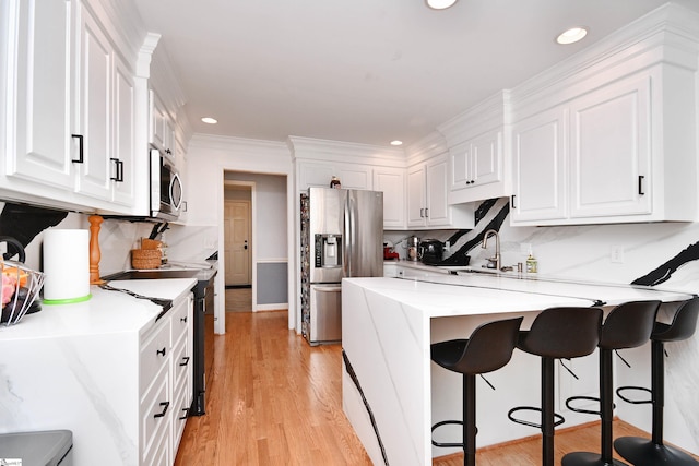 kitchen featuring a kitchen breakfast bar, light wood-type flooring, a peninsula, white cabinets, and stainless steel appliances