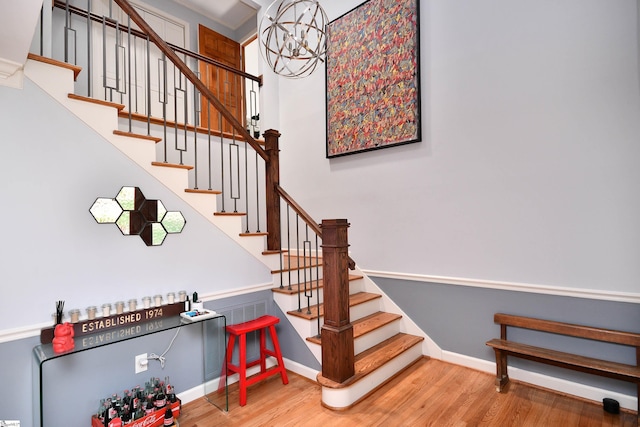 staircase featuring wood finished floors, an inviting chandelier, and baseboards