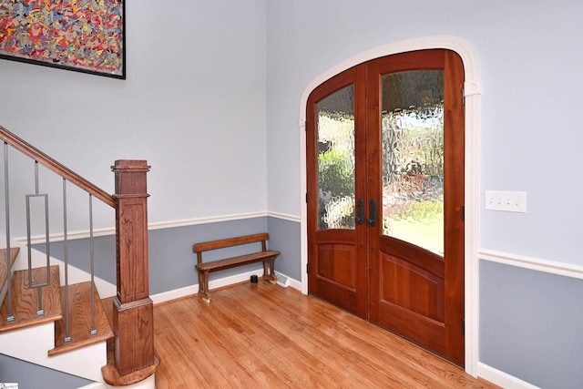 foyer with arched walkways, stairs, french doors, light wood finished floors, and baseboards
