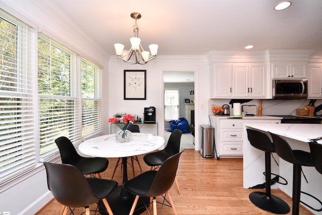 dining space featuring a healthy amount of sunlight, light wood finished floors, a notable chandelier, and ornamental molding