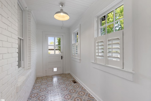 doorway featuring visible vents, a wealth of natural light, brick wall, and baseboards