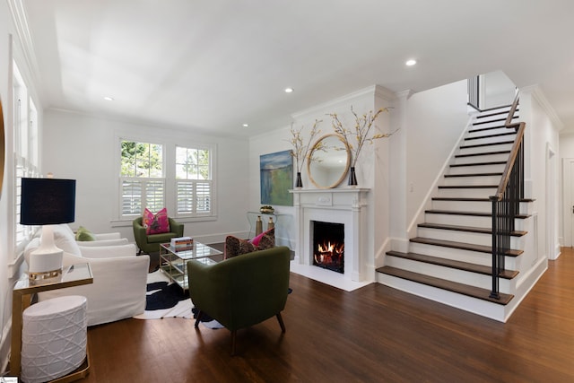living area with ornamental molding, stairs, wood finished floors, and a fireplace with flush hearth