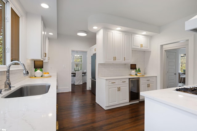 kitchen with dark wood finished floors, light stone countertops, white cabinetry, a sink, and wine cooler