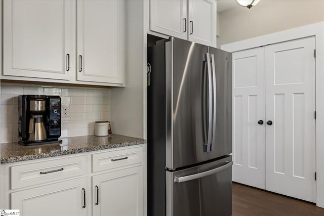 kitchen with dark stone counters, freestanding refrigerator, dark wood finished floors, tasteful backsplash, and white cabinets