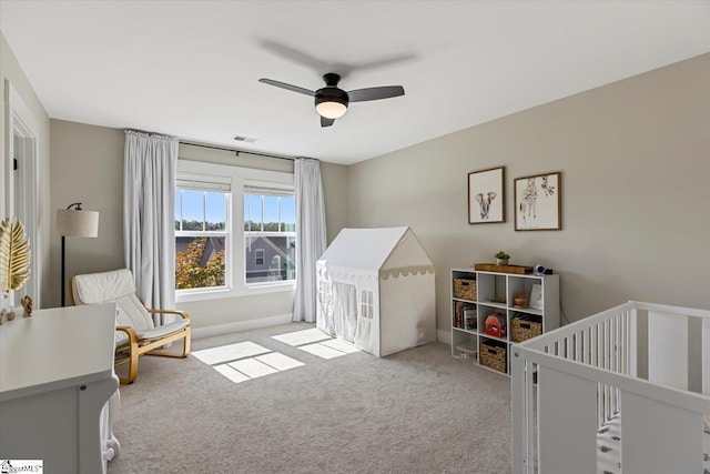 bedroom featuring visible vents, a ceiling fan, a crib, and light carpet