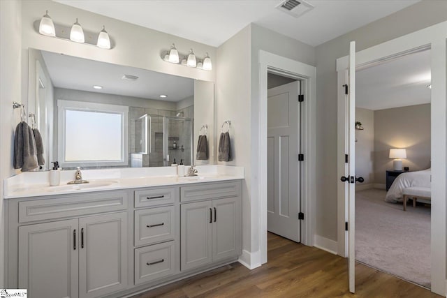 full bathroom with visible vents, a sink, a shower stall, double vanity, and wood finished floors
