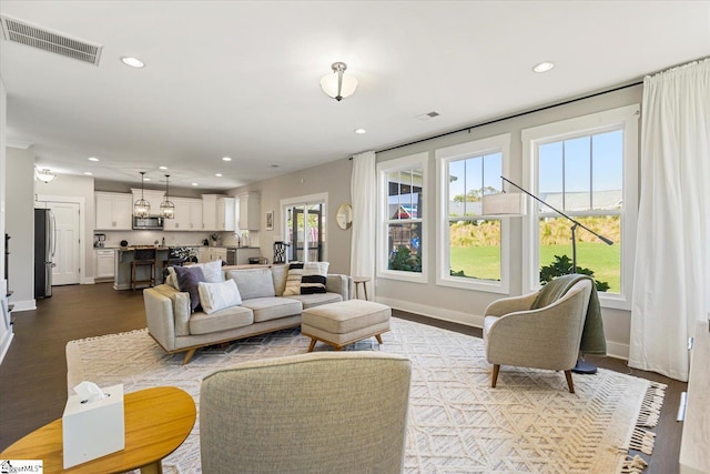 living room featuring dark wood-style flooring, baseboards, visible vents, and recessed lighting