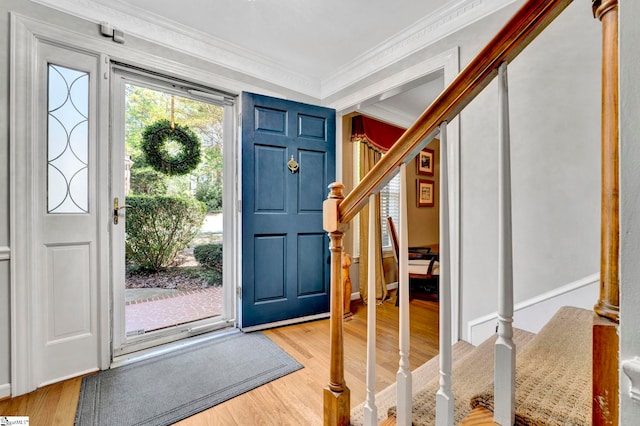 foyer featuring light wood-style flooring, crown molding, and stairs