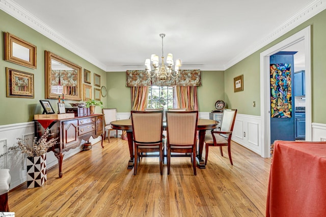 dining room featuring light wood-style floors, ornamental molding, an inviting chandelier, and a wainscoted wall