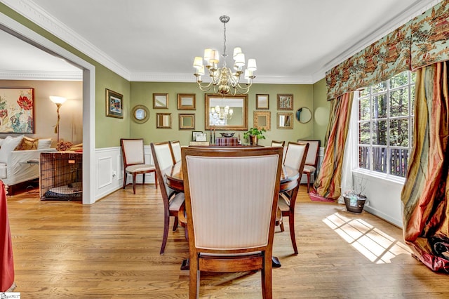 dining area featuring light wood-style floors, crown molding, a notable chandelier, and a wainscoted wall