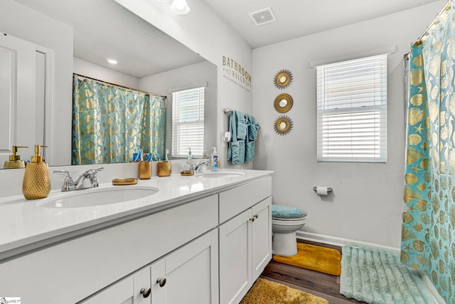full bath with double vanity, toilet, visible vents, a sink, and wood finished floors
