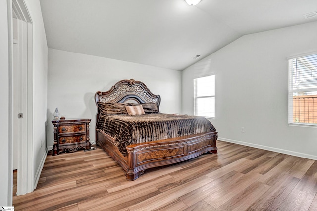 bedroom with light wood-type flooring, visible vents, baseboards, and vaulted ceiling