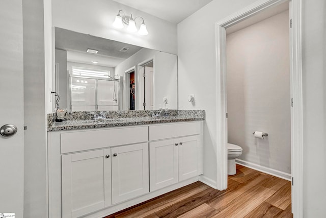 bathroom with baseboards, double vanity, toilet, a shower stall, and wood finished floors