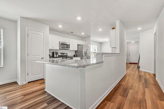 kitchen featuring a peninsula, white cabinetry, light wood-type flooring, and stainless steel appliances