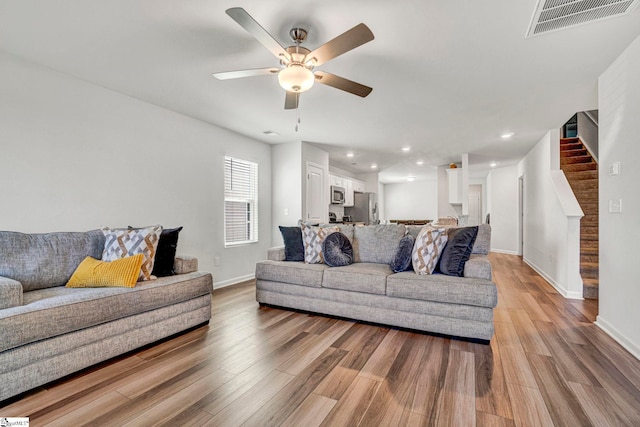 living room with stairs, visible vents, light wood-type flooring, and a ceiling fan
