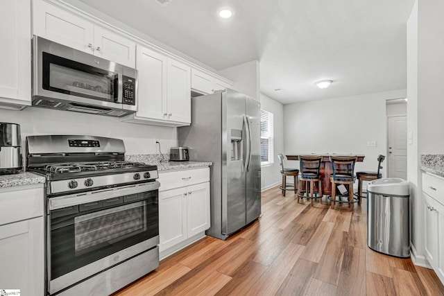 kitchen featuring light stone countertops, appliances with stainless steel finishes, light wood finished floors, and white cabinets