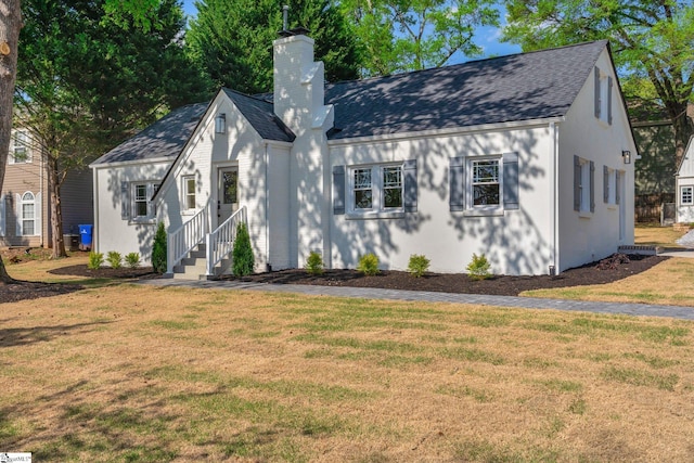 view of front facade with roof with shingles, a front lawn, and a chimney