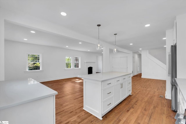 kitchen featuring open floor plan, a brick fireplace, white cabinetry, and light wood-style flooring