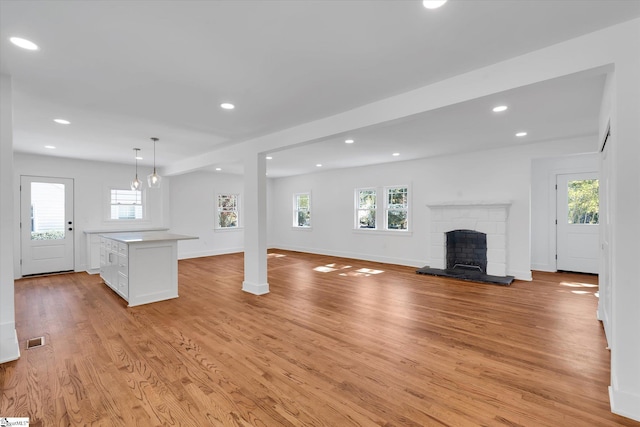 unfurnished living room with light wood-type flooring, plenty of natural light, a fireplace with raised hearth, and recessed lighting