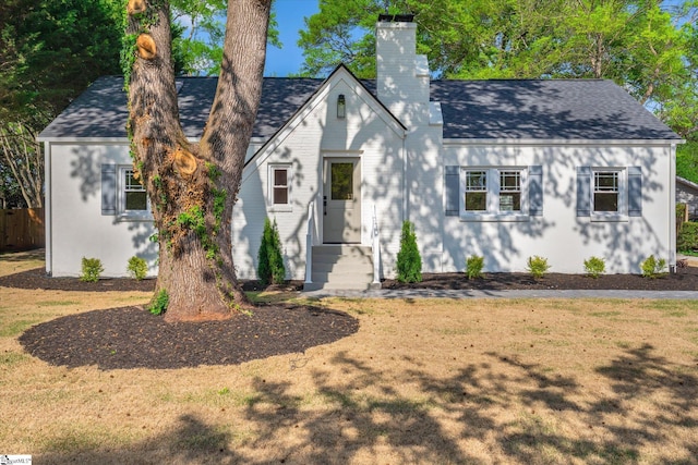 tudor home featuring fence, a front lawn, a chimney, and a shingled roof