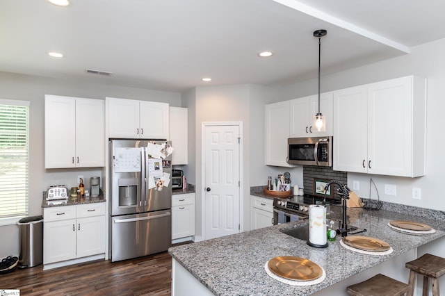 kitchen with visible vents, dark wood-style flooring, appliances with stainless steel finishes, a peninsula, and stone countertops