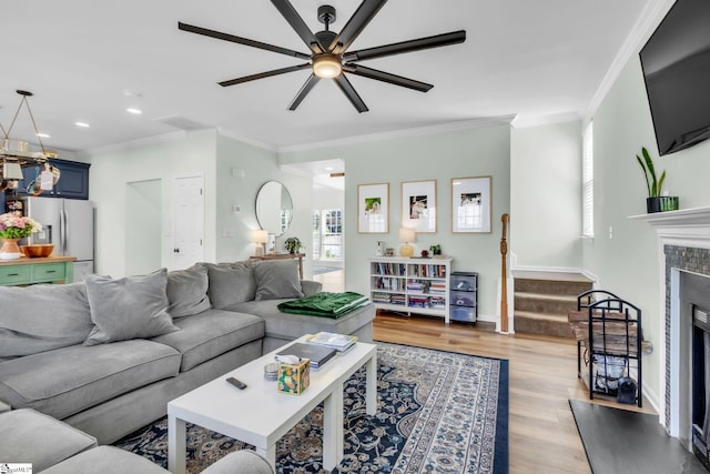 living area with a healthy amount of sunlight, ceiling fan, a tiled fireplace, and stairs