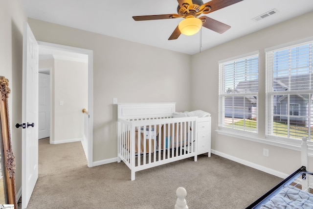 carpeted bedroom with visible vents, baseboards, a nursery area, and ceiling fan