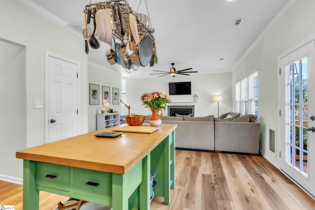 kitchen with green cabinets, a fireplace, crown molding, and butcher block counters
