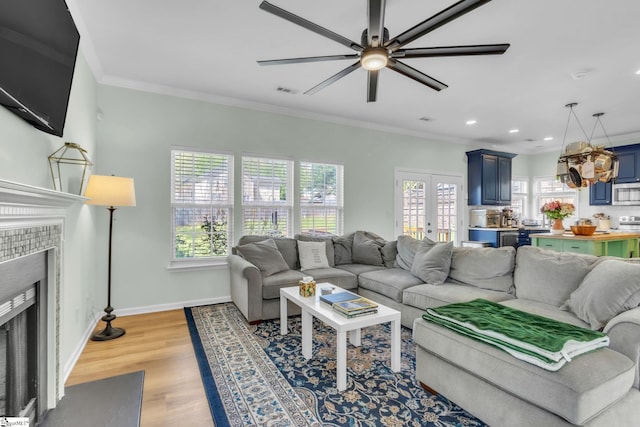 living room with baseboards, ornamental molding, a ceiling fan, a fireplace with flush hearth, and light wood-style floors