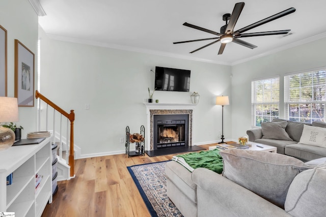 living area with a fireplace with raised hearth, ornamental molding, ceiling fan, stairway, and wood finished floors