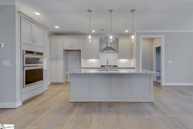 kitchen featuring wall chimney range hood, tasteful backsplash, stainless steel appliances, and light wood finished floors
