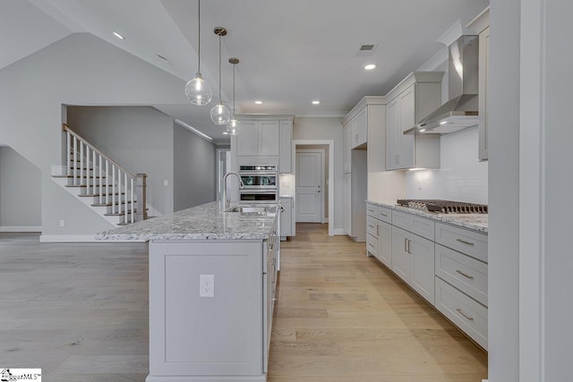 kitchen featuring visible vents, wall chimney exhaust hood, light wood finished floors, stainless steel appliances, and decorative backsplash